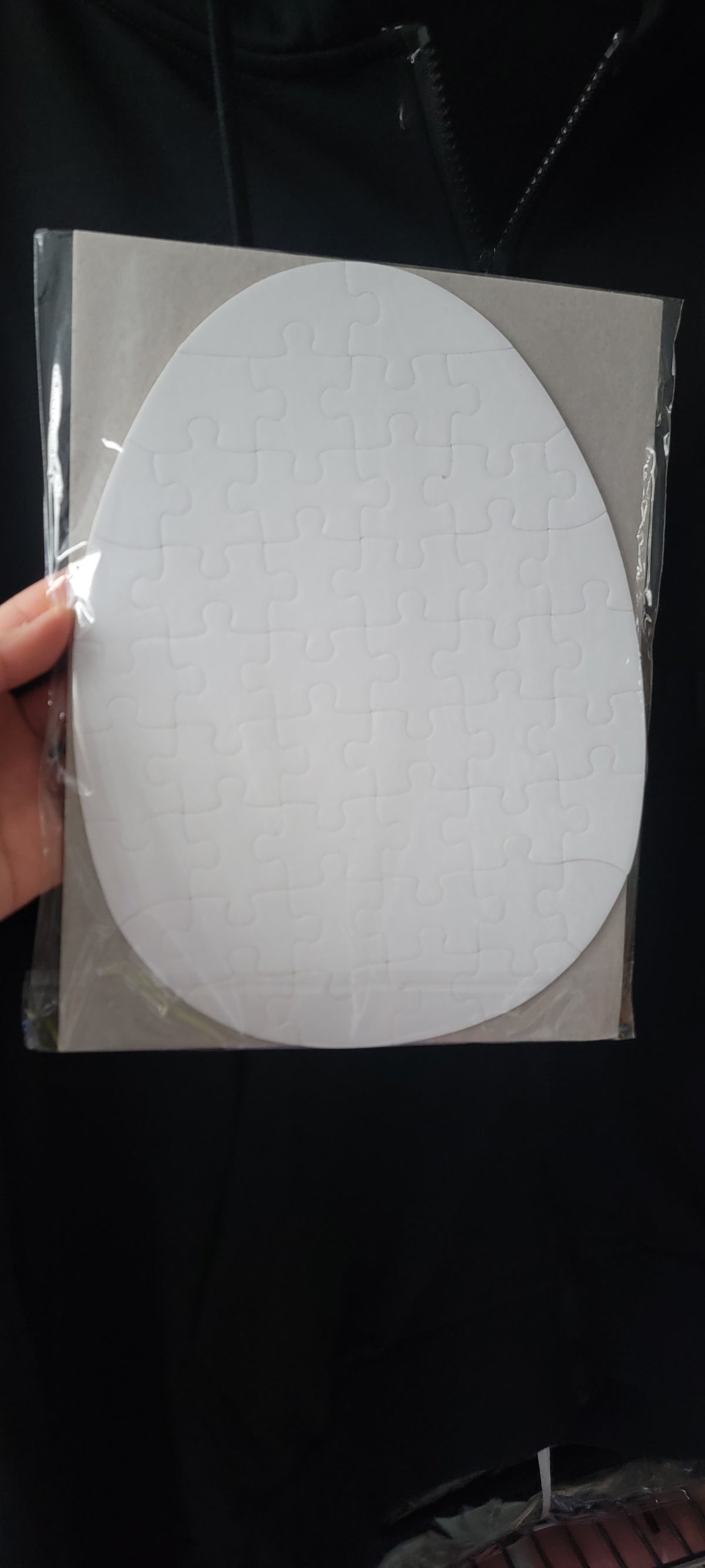 Sealed white egg-shaped 51-piece sublimation puzzle blank held against a dark background